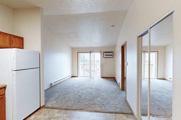 A white refrigerator is in the corner of a room with a carpeted floor.
