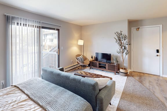 A bedroom with a bed, a couch, a television, and a window with blinds.
