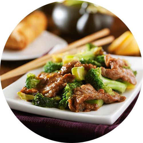 A plate of beef and broccoli with chopsticks on the side.