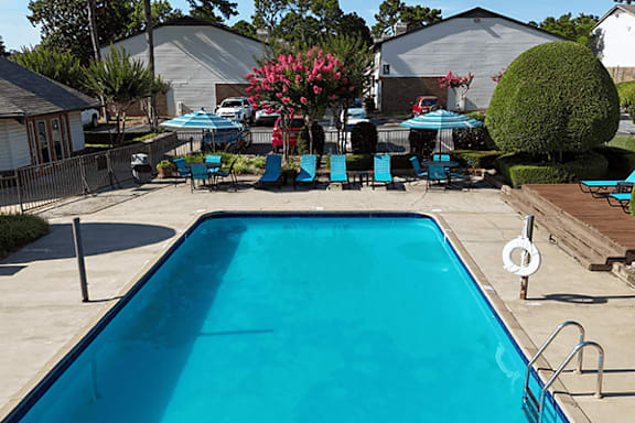 A blue swimming pool in a backyard with a deck and chairs.