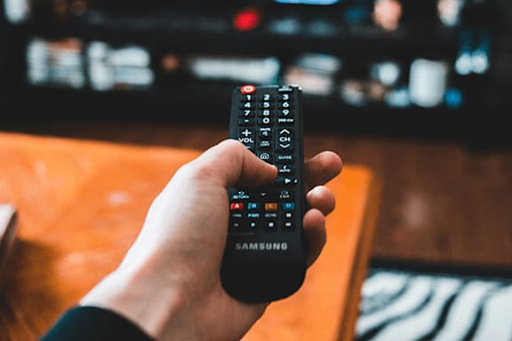 A person is holding a Samsung remote control in front of a television.