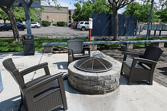 A fire pit surrounded by chairs in a sunny outdoor setting.