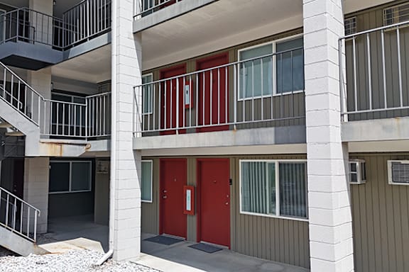 A red door is on the ground floor of a white and grey building.