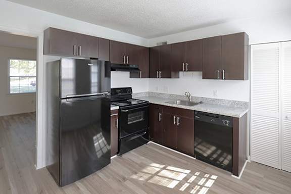 A kitchen with dark brown cabinets and a black fridge.