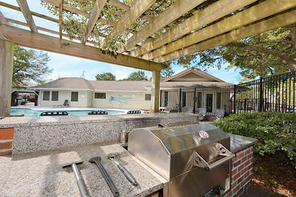 A BBQ grill is in the foreground of a backyard with a pool and houses in the background.