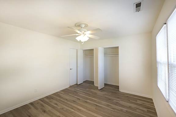 A bedroom with a ceiling fan and wooden flooring.