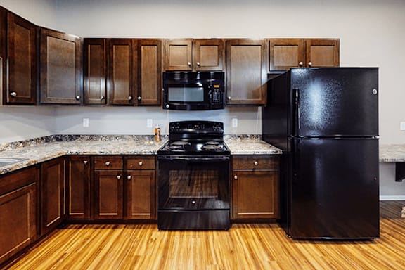 A black refrigerator sits next to a black stove in a kitchen with wooden cabinets.