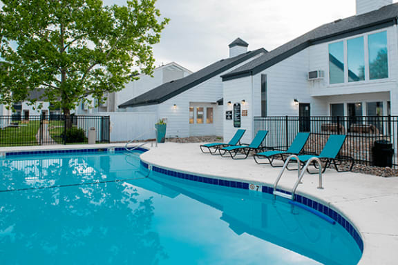 a swimming pool with blue chaise lounge chairs and a building in the background