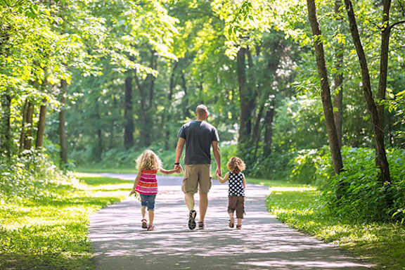 A man and two children are walking down a path in a green forest.