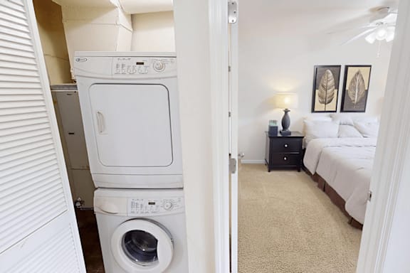 A white dryer is in a small room with a bed and a nightstand.