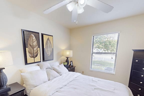 A bedroom with a bed, two lamps, and two framed leaves on the wall.