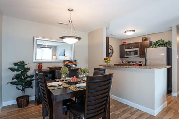 a dining room table with chairs next to a kitchen with a refrigerator and sink
