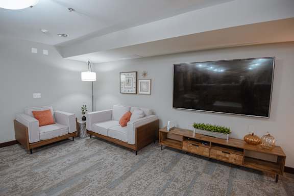A living room with a grey carpet and a television on the wall.