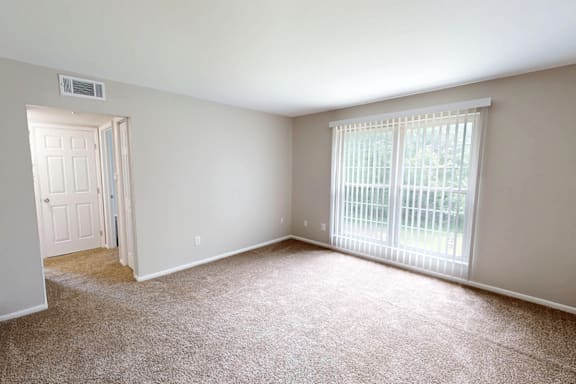 A room with a carpeted floor and a window with blinds.