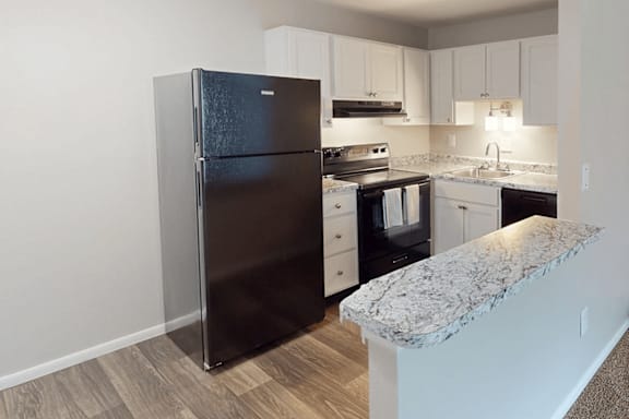A black refrigerator stands in a kitchen with a marble counter.