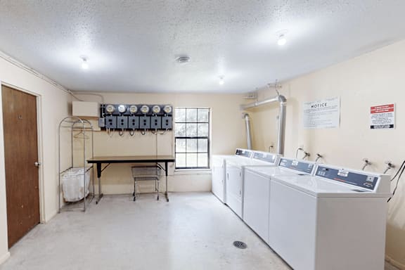 A room with a white ceiling and walls, containing a sink, a table, and a window.
