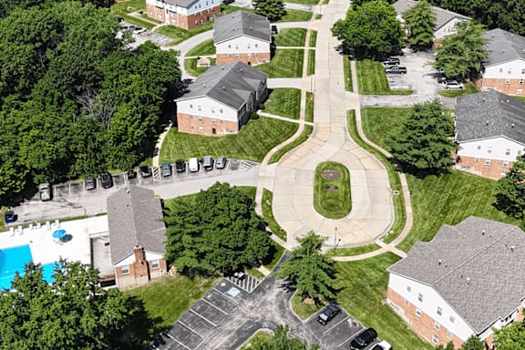 A bird's eye view of a residential area with houses, trees, and a pool.