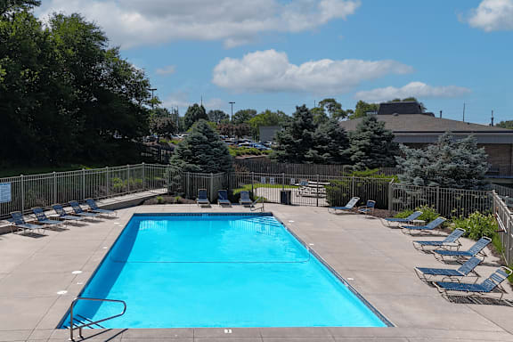 A large blue swimming pool surrounded by a fence and lounge chairs.
