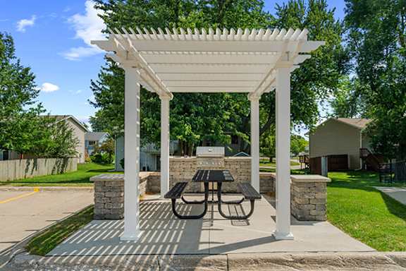 A white pergola with a table and chairs is set up in a park.