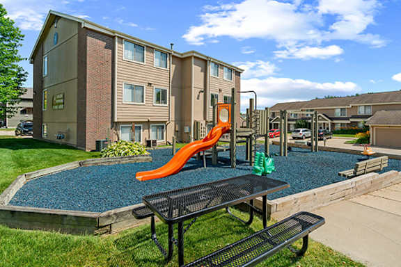 A playground area with a slide and picnic table in front of apartment buildings.