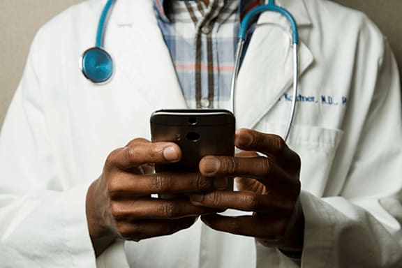 A doctor in a white coat is holding a smartphone.