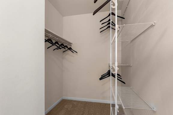 A white closet with clothes hanging on hangers.