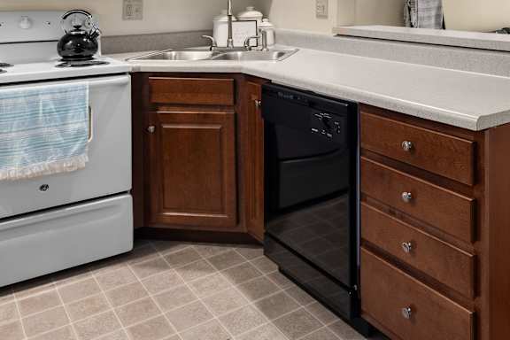 A kitchen with a white stove, a black dishwasher, and a wooden cabinet.