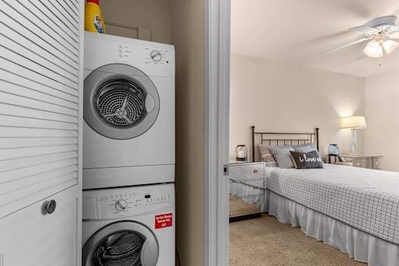 A white washing machine is in a small room with a bed.