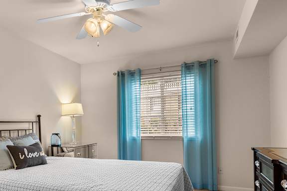 A bedroom with a bed, a ceiling fan, and a nightstand with a lamp.