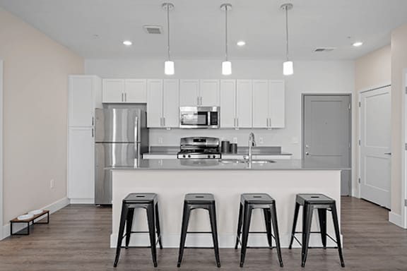 A kitchen with white cabinets and a white island with four black stools.