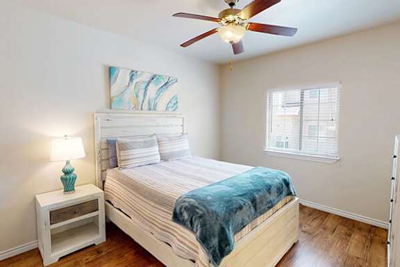 A bedroom with a bed, a ceiling fan, and a nightstand with a lamp.