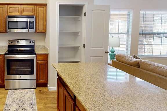 A kitchen with a stove, microwave, and an empty refrigerator.