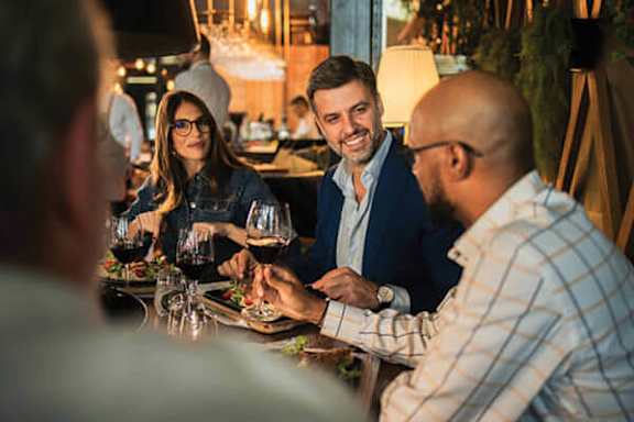 A group of people are sitting around a table enjoying a meal and drinks.