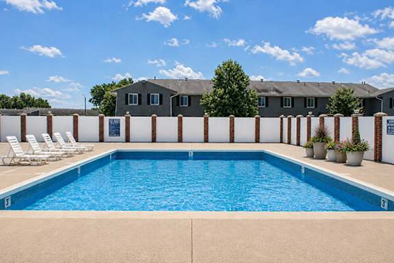 A swimming pool with chairs and a building in the background.