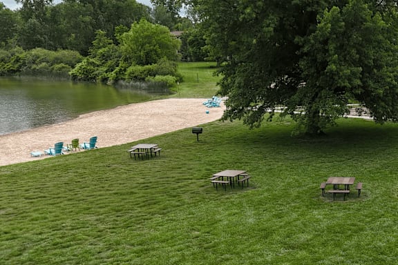 A park with picnic tables and chairs by a lake.