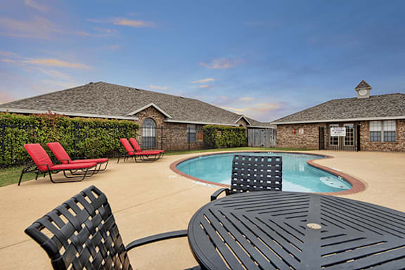 A black table and chairs are in the foreground of a backyard with a pool and houses in the background.