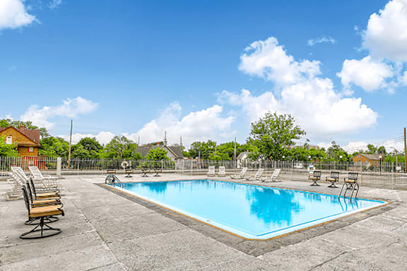 A swimming pool surrounded by chairs and trees.
