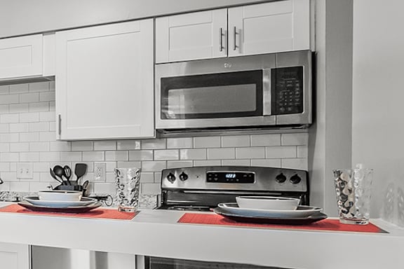A black and white photo of a kitchen with a microwave, toaster oven, and a red placemat on the counter.