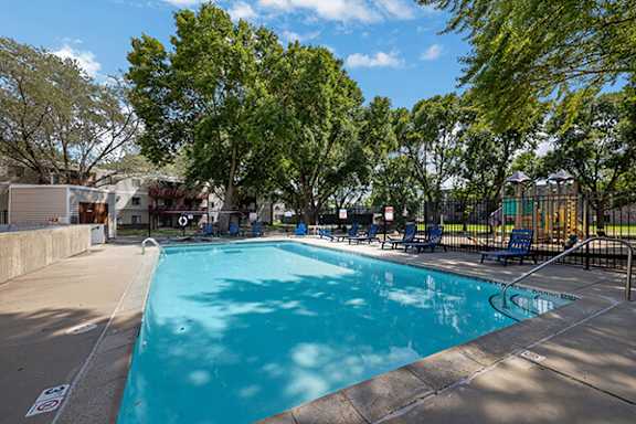 A large swimming pool surrounded by trees and lounge chairs.