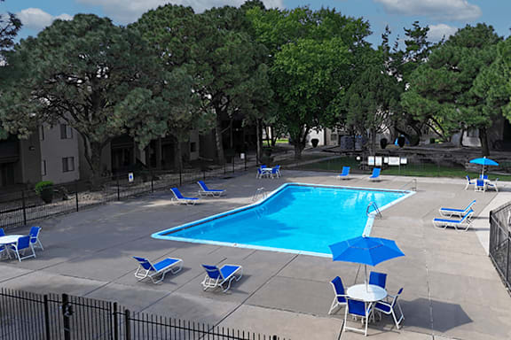 A pool surrounded by trees and chairs.