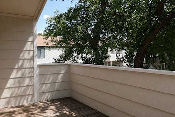 A balcony with a white wall and a tree in the background.