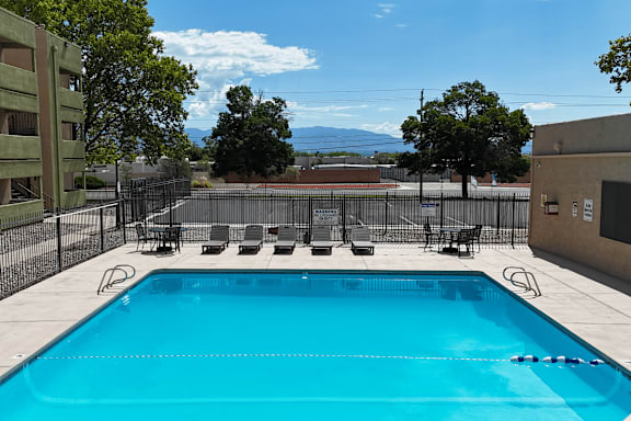 A blue swimming pool surrounded by a fence and chairs.