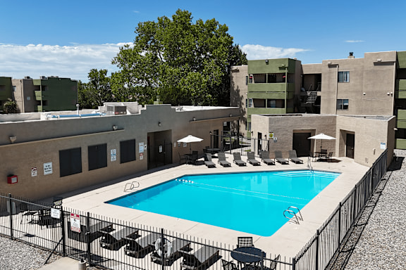 A pool surrounded by a black fence and chairs.