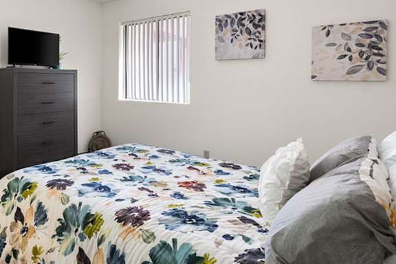 A bed with a floral comforter and pillows sits in a room with a television and two wall art pieces.