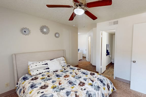 A bedroom with a floral bedspread and a ceiling fan.