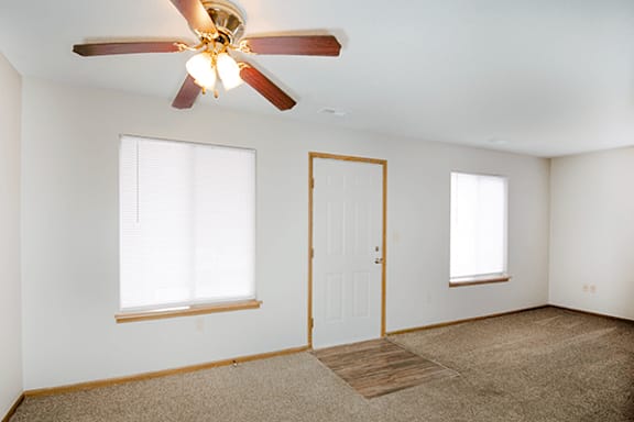 A room with a ceiling fan and two windows.