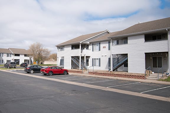 A red car is parked in a parking lot in front of a white building.