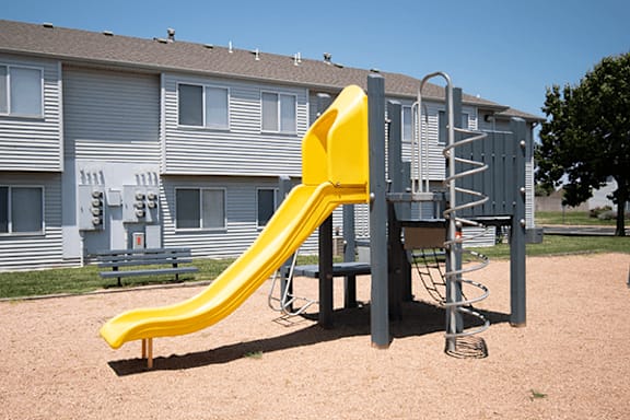 A yellow slide in a playground with a building in the background.