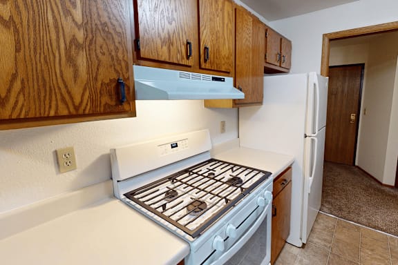 A kitchen with a white stove top oven and wooden cabinets.