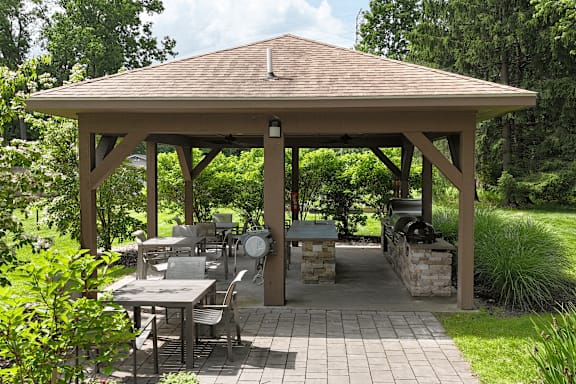 A gazebo with a table and chairs is surrounded by greenery.